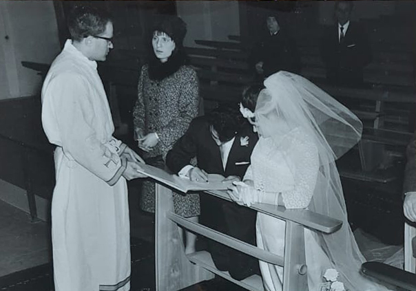 La fotografia ritrae Giovanni Villella in Chiesa, inginocchiato accanto la moglie in abito da sposa, nel momento della firma dell’atto di matrimonio. Il prete, con accanto una testimone di nozze, regge il libro. Sullo sfondo si intravedono alcuni invitati alla cerimonia.