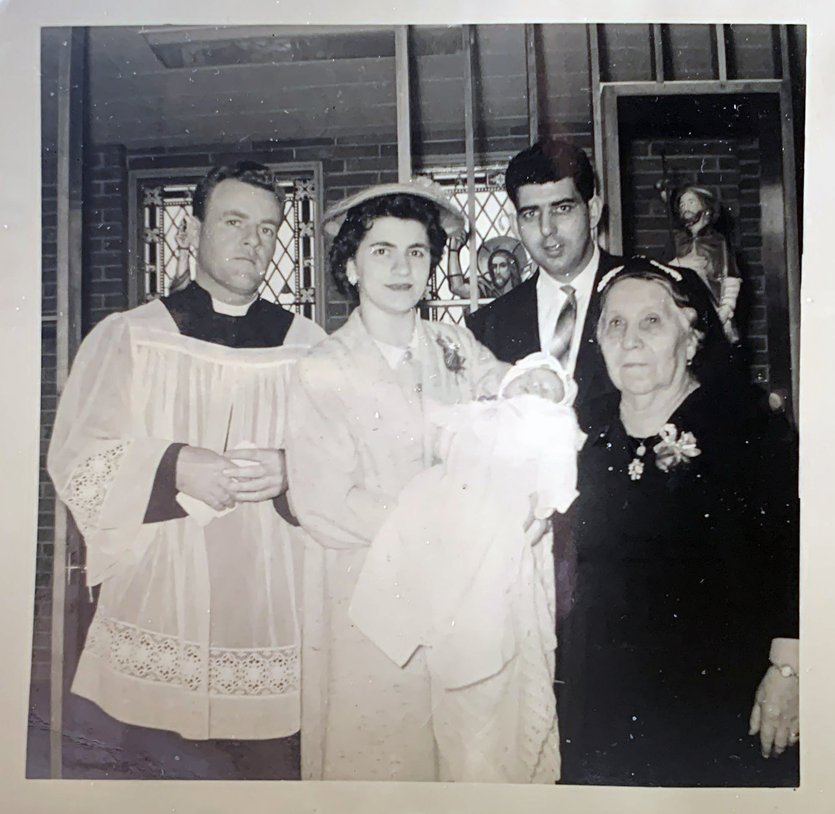 Questa foto ritrae una famiglia italiana emigrata negli Stati Uniti d’America e inviata a Conflenti, paese calabrese in provincia di Catanzaro, come ricordo di un battesimo. La madre regge in braccio la bambina vestita in abito rituale da battesimo con alla sua destra il prete e alla sua sinistra la madre, dietro posa il marito.